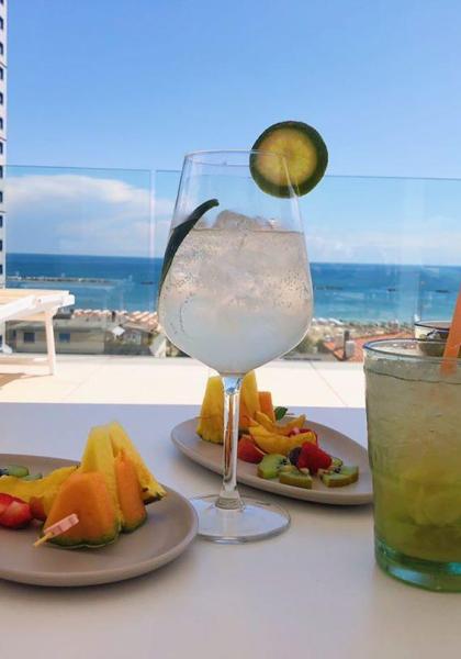 Cocktails et fruits avec vue sur la mer sur une terrasse ensoleillée.