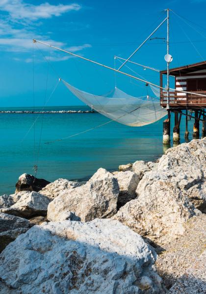 Casetta sul mare con rete da pesca e cielo azzurro.