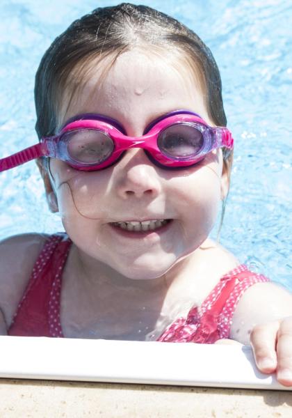 Bambina in piscina con occhialini rosa, sorridente.