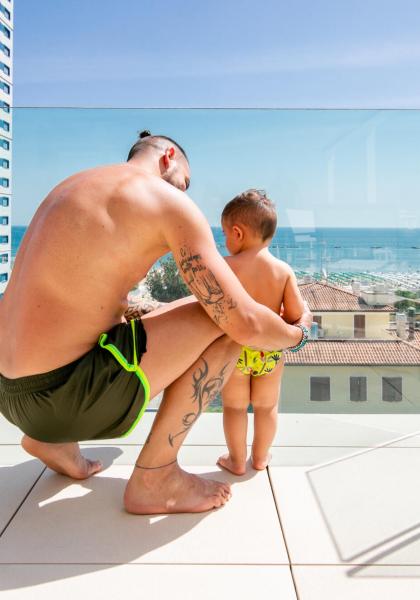 Père et fils sur une terrasse avec vue sur la mer, journée ensoleillée.