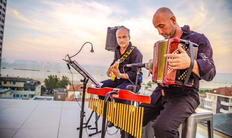 Musikduo spielt auf Dachterrasse bei Sonnenuntergang, mit Akkordeon und Gitarre.