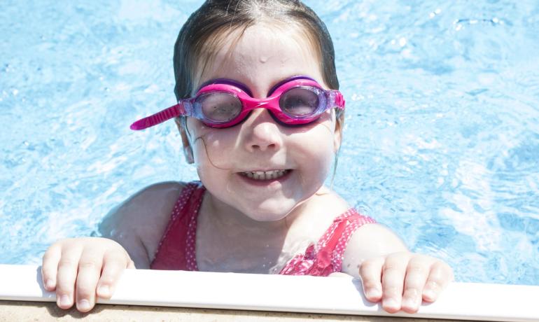 Fille dans la piscine avec lunettes roses, souriante.